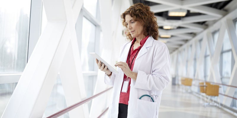 Physician standing in hallway looking at ipad.