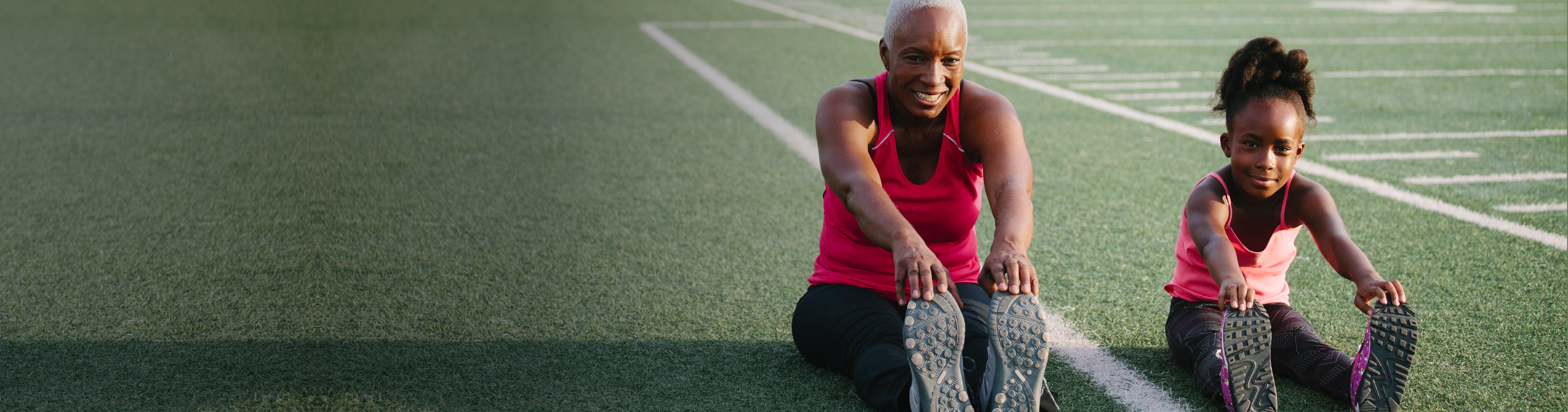 Grandmother and granddaughter stretching on a football field.