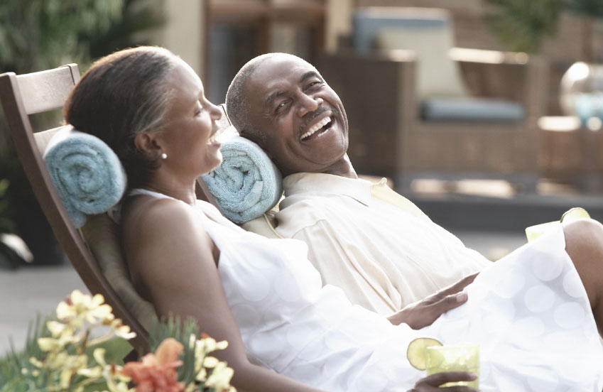 Couple laughing and sitting on lounge chairs with towels behind their necks.