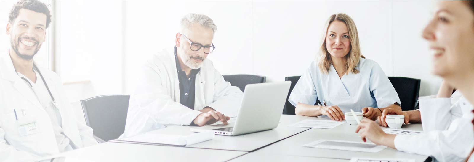 Group of medical professionals seated at a meeting table smiling with laptop.