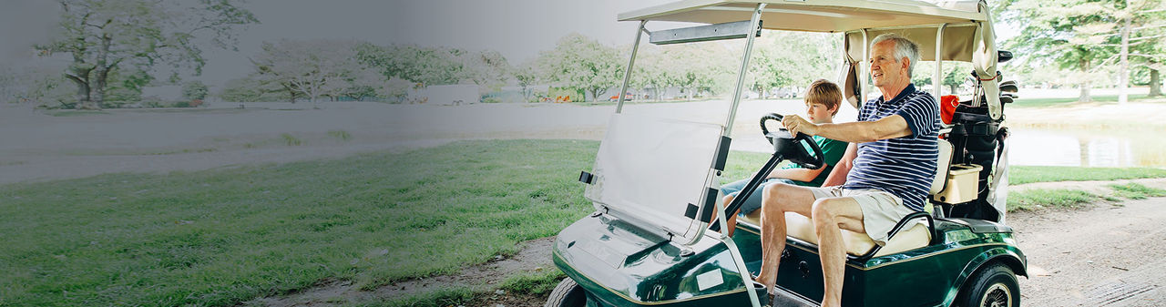 Senior man driving golf cart with young boy.
